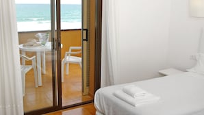 A hotel room with a bed, a small table with chairs, and a view of the ocean through a glass door. - Apartamentos Beach & Golf Resort (Pals)