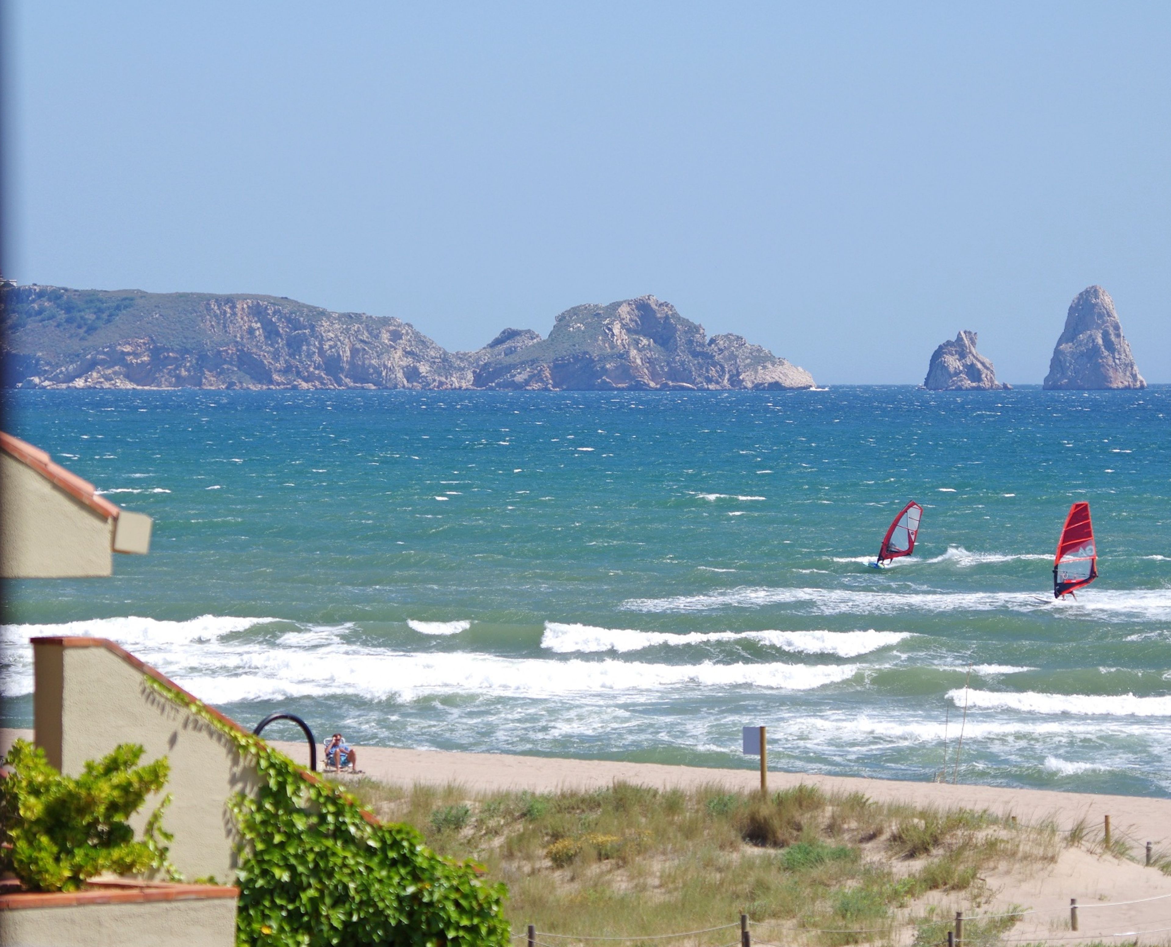 Blick auf die Küste mit Windsurfern, felsigen Klippen und einem Sandstrand.