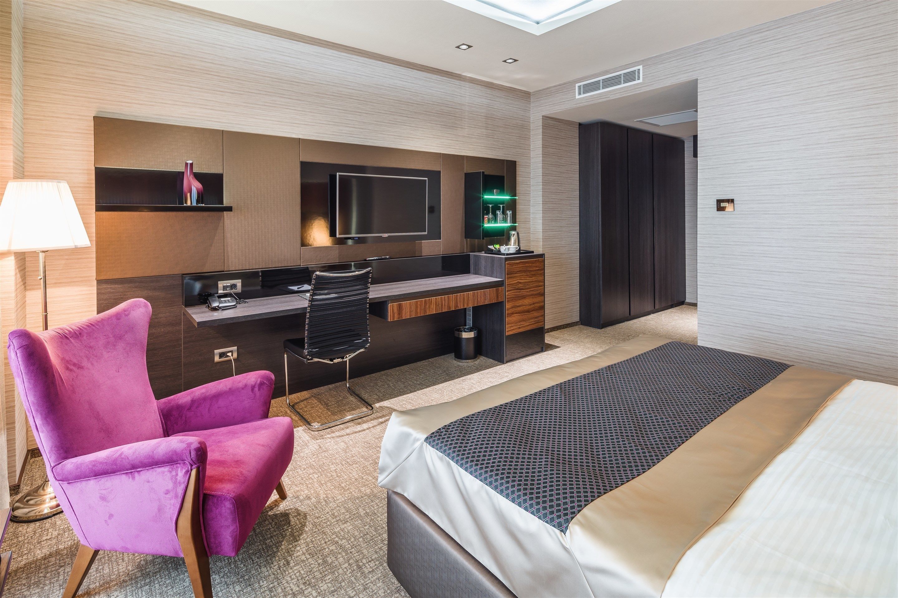 A modern hotel room with a bed, a desk, a chair, and a TV.