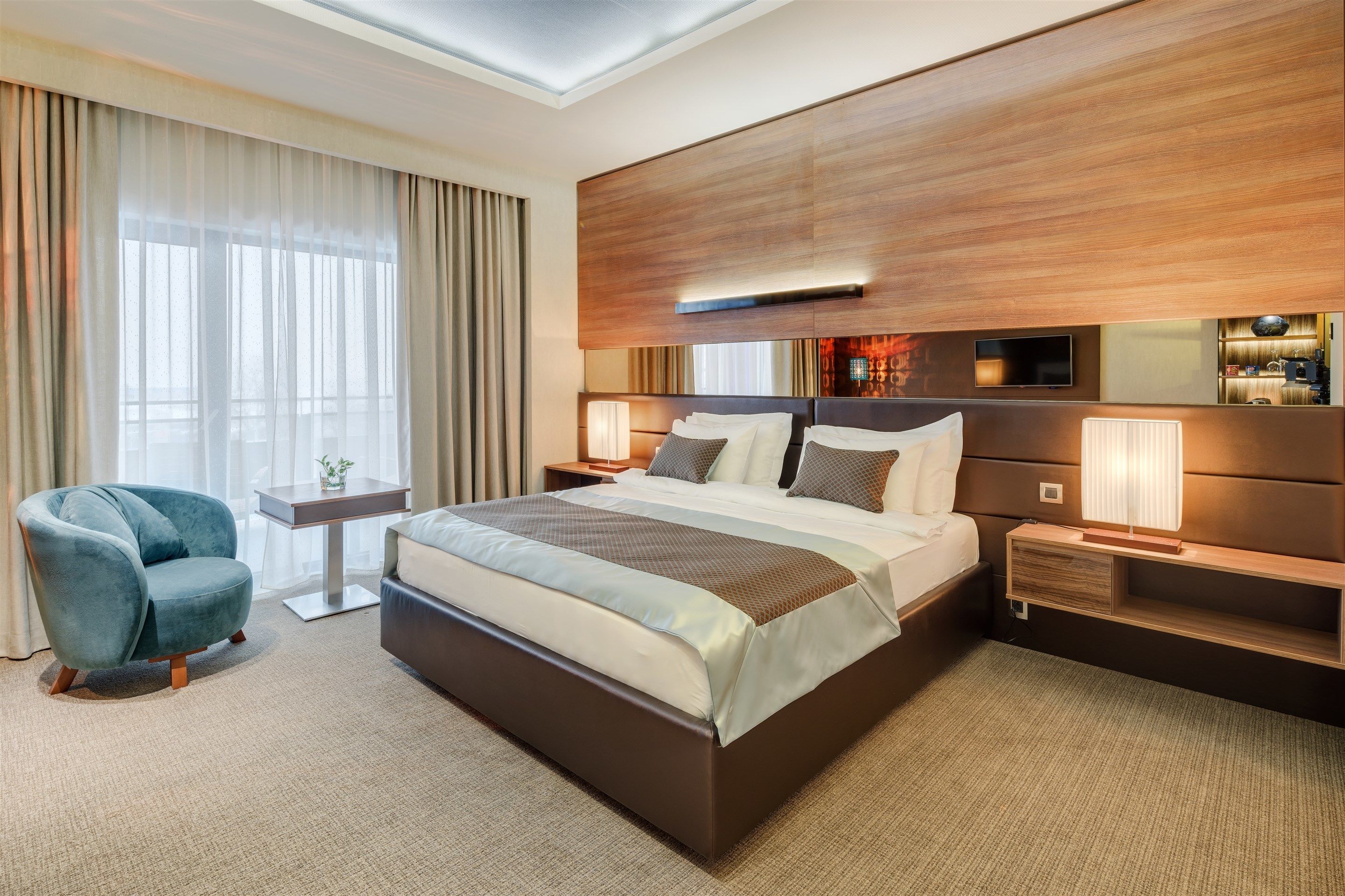 Una habitación de hotel moderna con una cama grande, una zona de estar con una silla, una mesita de noche y un televisor.