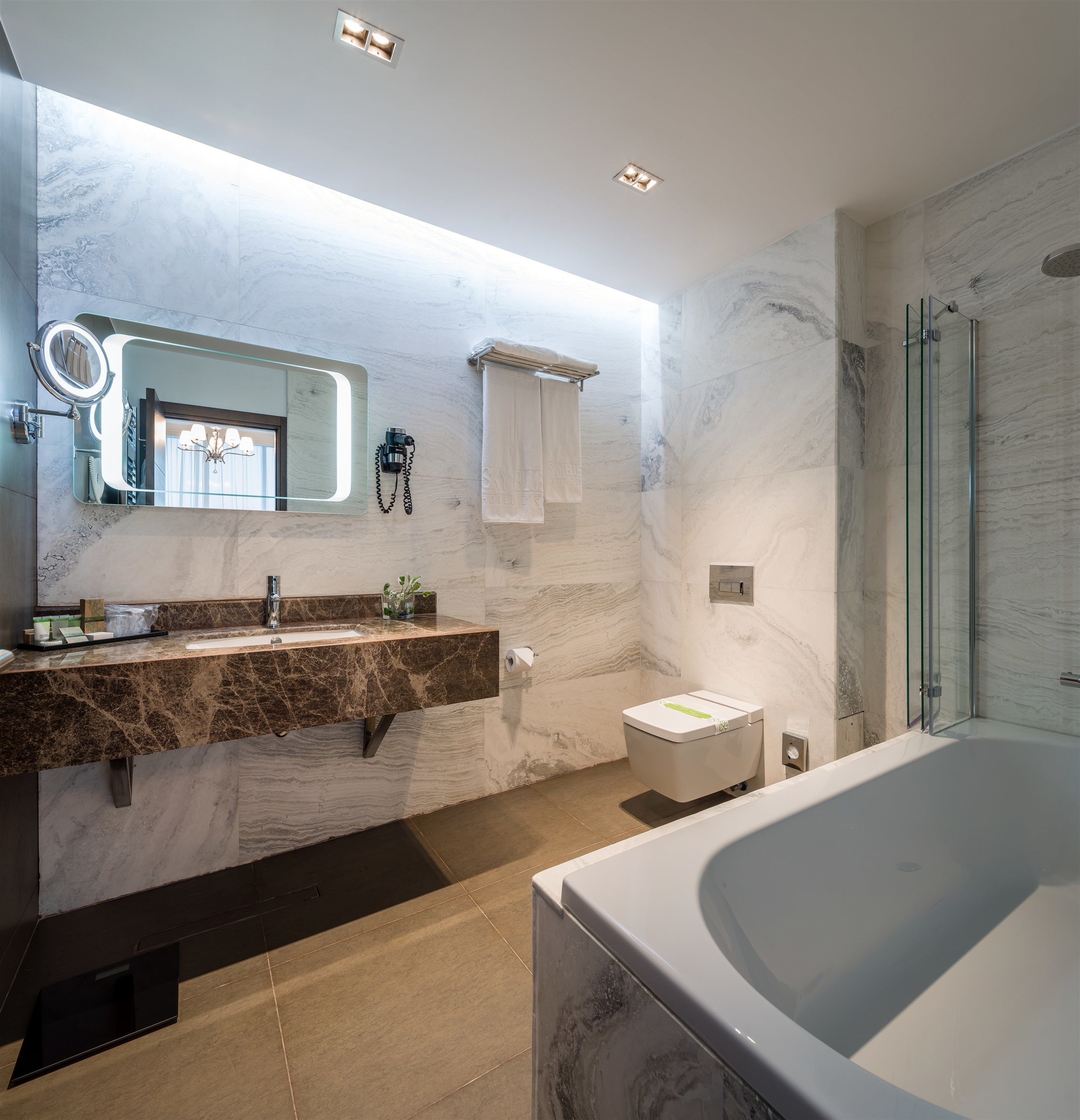 A modern bathroom with a marble vanity, a large mirror, a glass shower enclosure, and a bathtub.