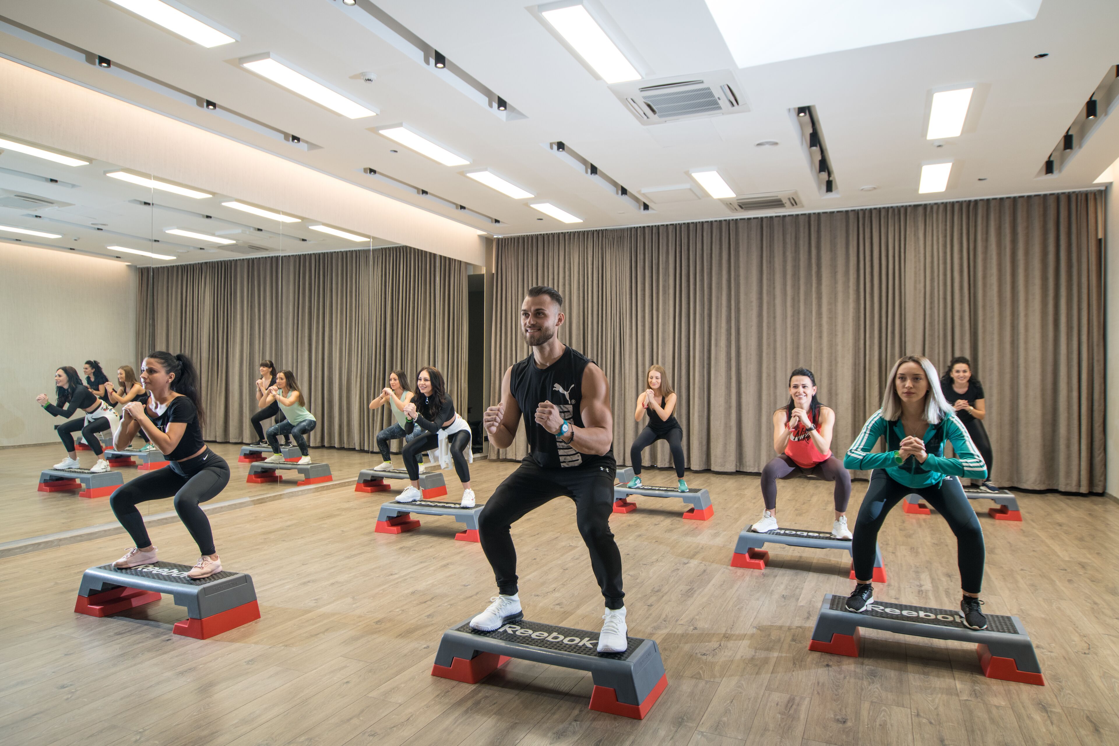 A fitness class in a well-lit room with wooden floors and a large mirror on one wall.