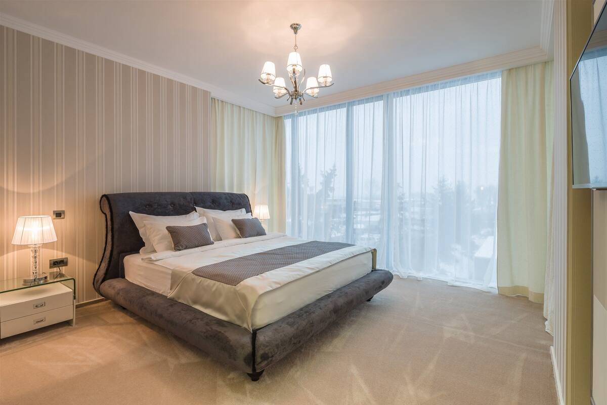Um quarto espaçoso com uma cama grande, uma mesa de cabeceira com abajur e um lustre.