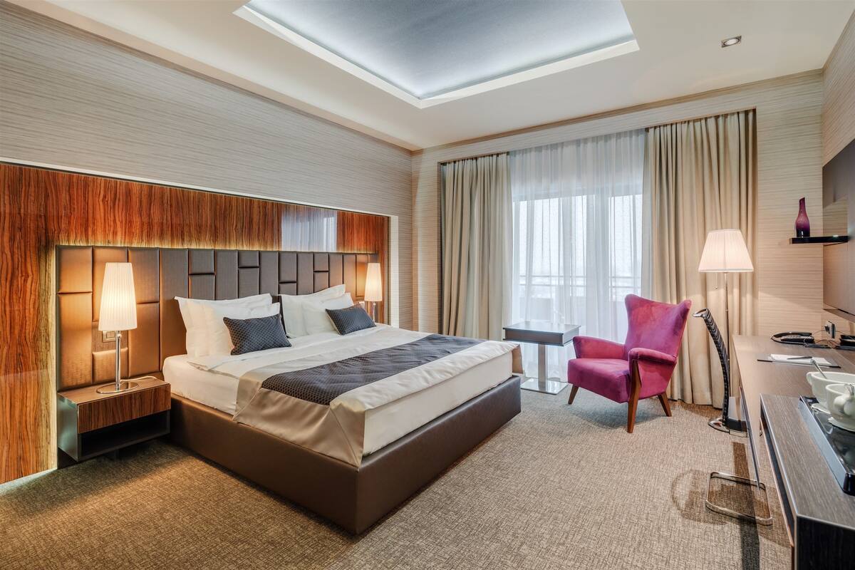 Quarto de hotel moderno com uma cama grande, mesas de cabeceira, uma escrivaninha e uma cadeira.