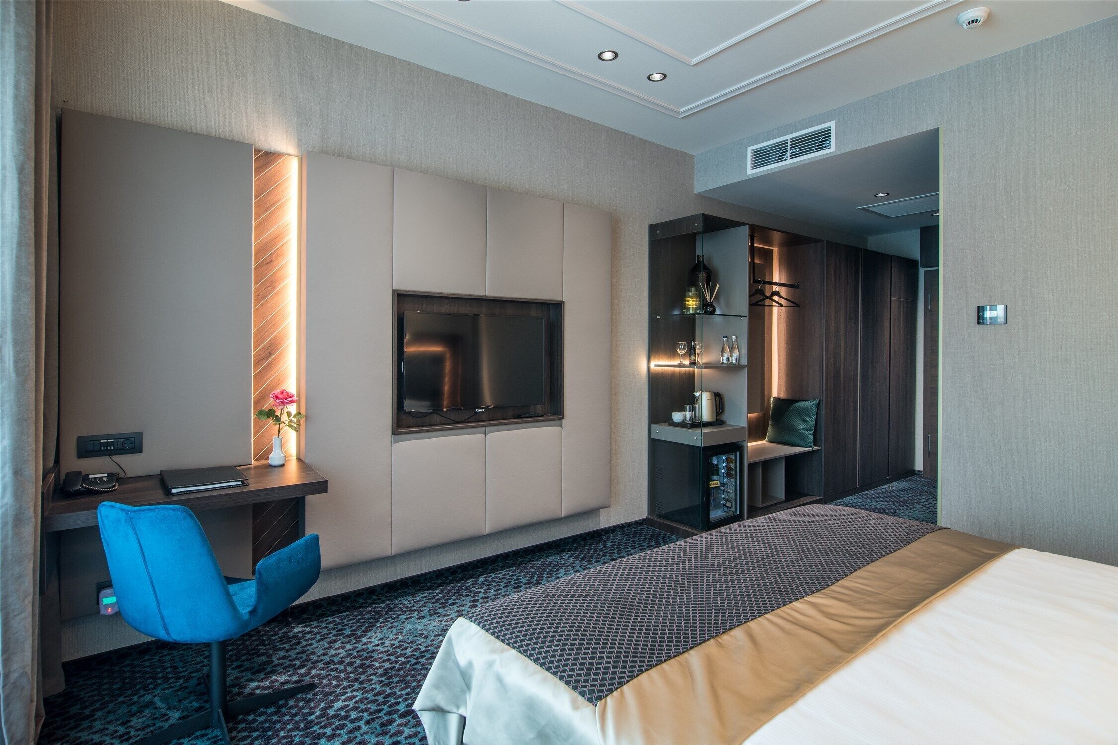 Een hotelkamer met een bed, een bureau met stoel, een televisie en een minibar.