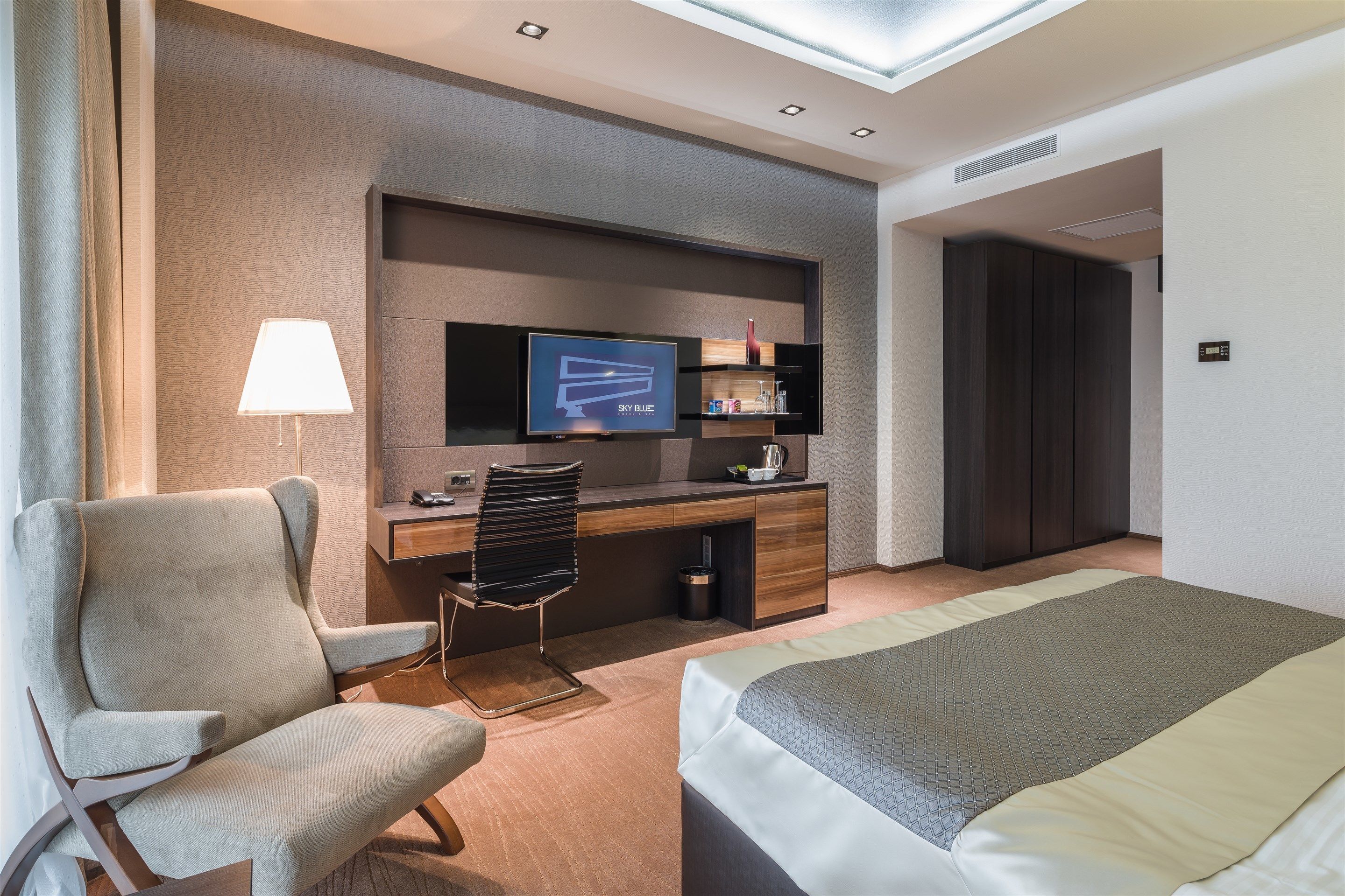 A hotel room with a bed, a desk with a TV, a chair, and a lamp.