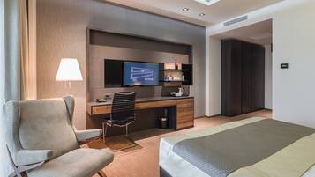 A hotel room with a bed, a desk with a TV, a chair, and a lamp.