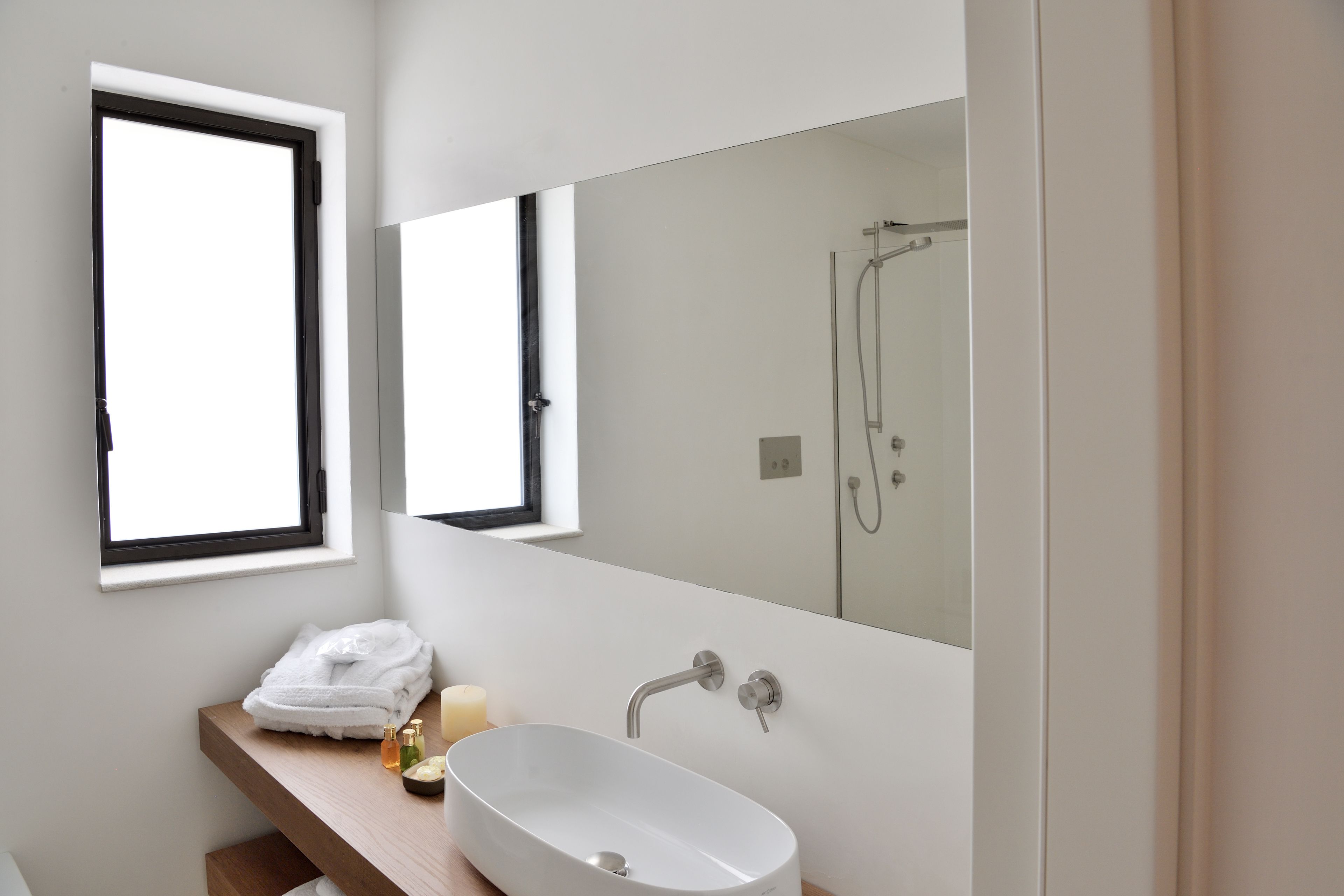 Un bagno moderno con uno specchio grande, un lavandino bianco e una doccia.