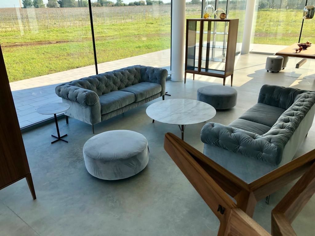 Ein großzügiger Wohnbereich mit grauem Sofa, runder Ottoman und einer Glaskabine.