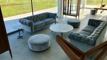 Un vaste espace de vie comprenant un canapé gris, un pouf rond et une vitrine.
