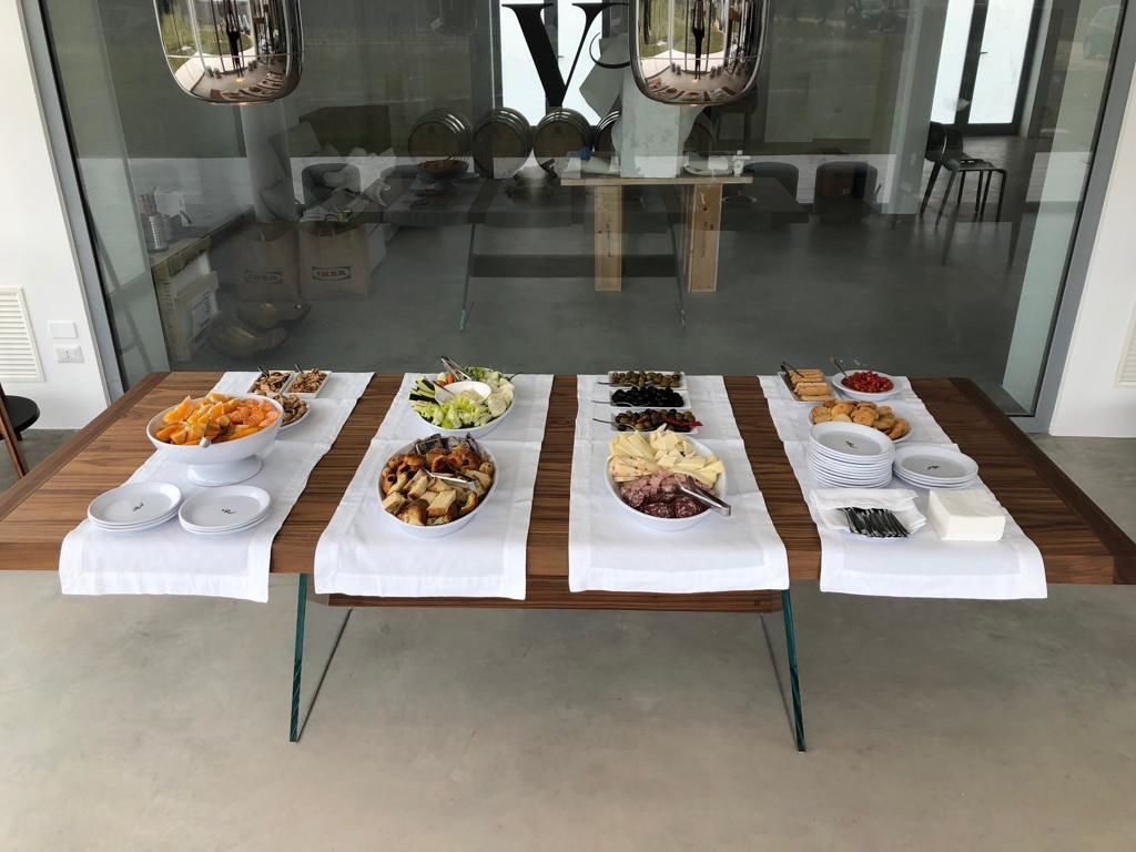 A buffet table with various dishes and plates set up in a modern dining area with glass walls and metal chairs.