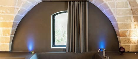 Un baño moderno con una bañera grande, una ventana con cortinas y un arco de piedra.