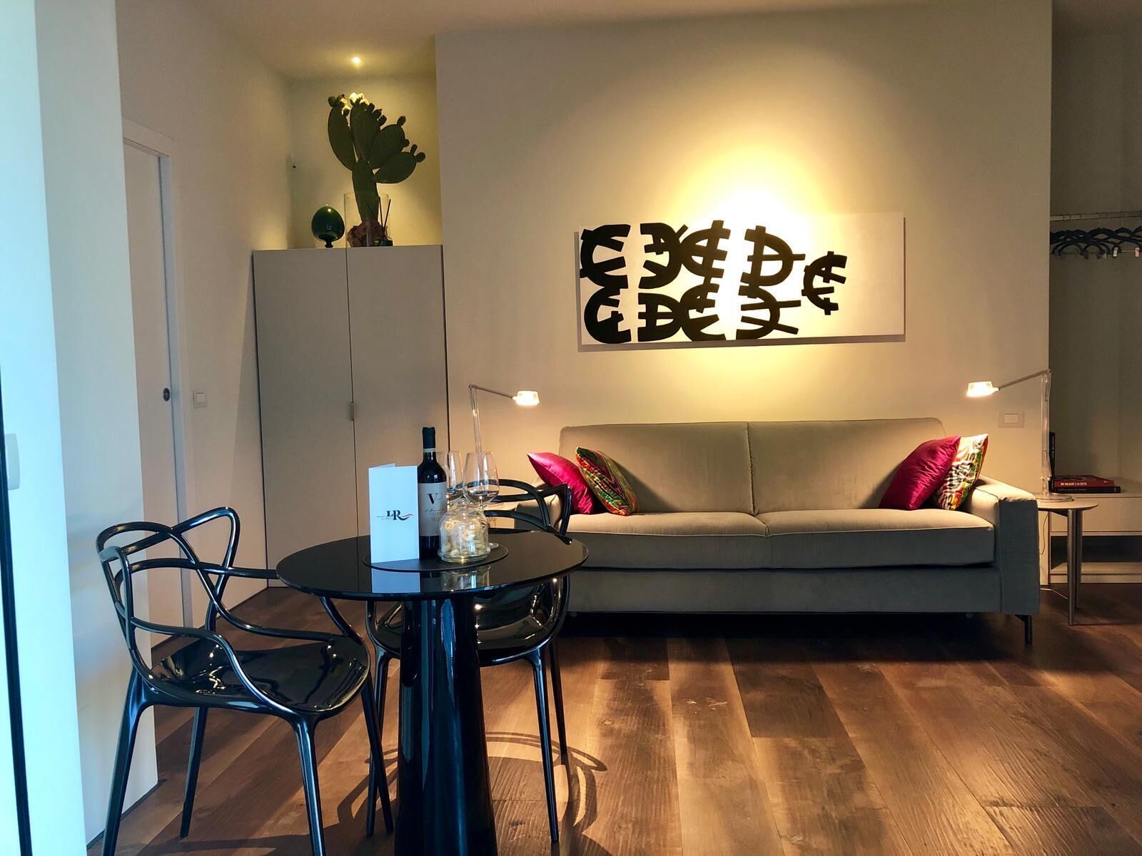 Ett modernt vardagsrum med ett runt bord, två stolar, en soffa med färgglada kuddar, en kaktus på en hylla och en vägg med stor text.