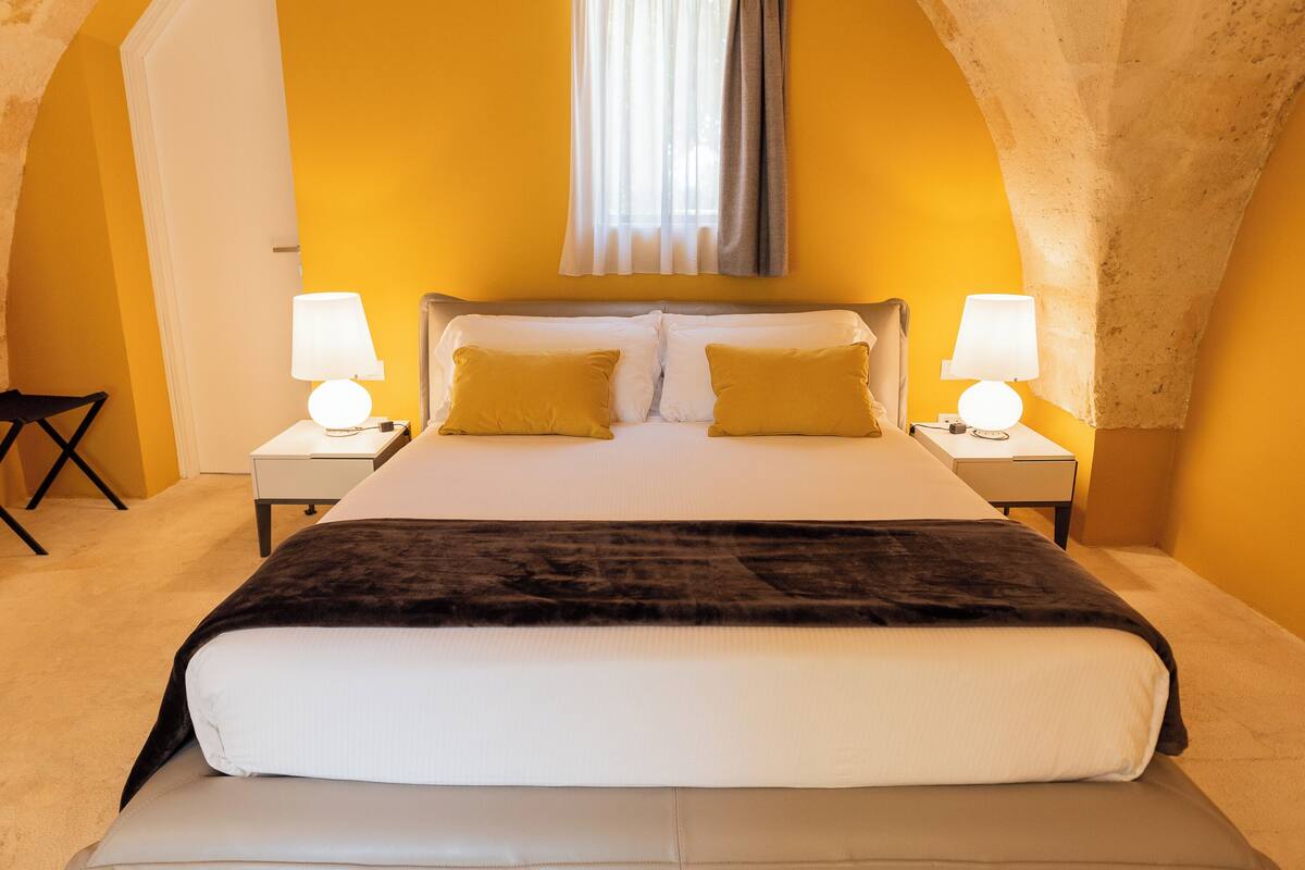 Ein Hotelzimmer mit einem großen Bett, zwei Nachttischen mit Lampen, einem Sessel und einem Fenster mit Vorhängen.
