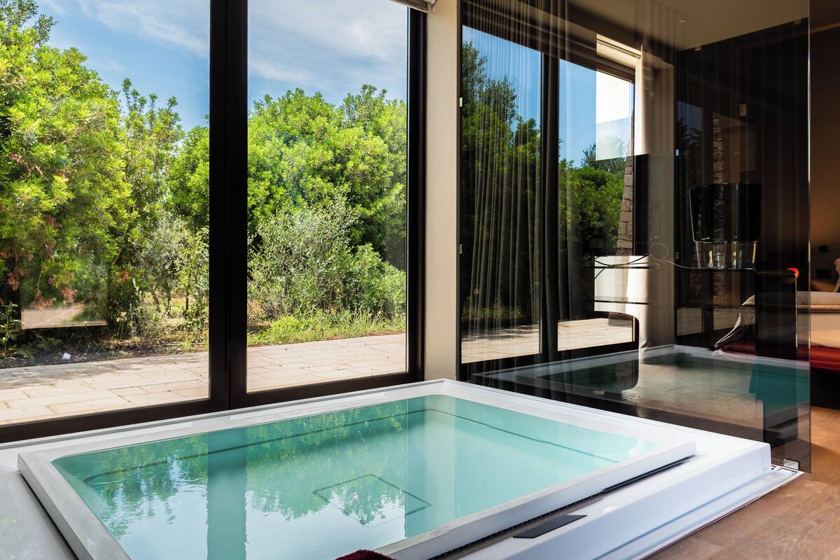 Ein modernes Hallenbad mit klaren Glaswänden, Blick auf üppiges Grün im Außenbereich und einem minimalistischen Interieur.