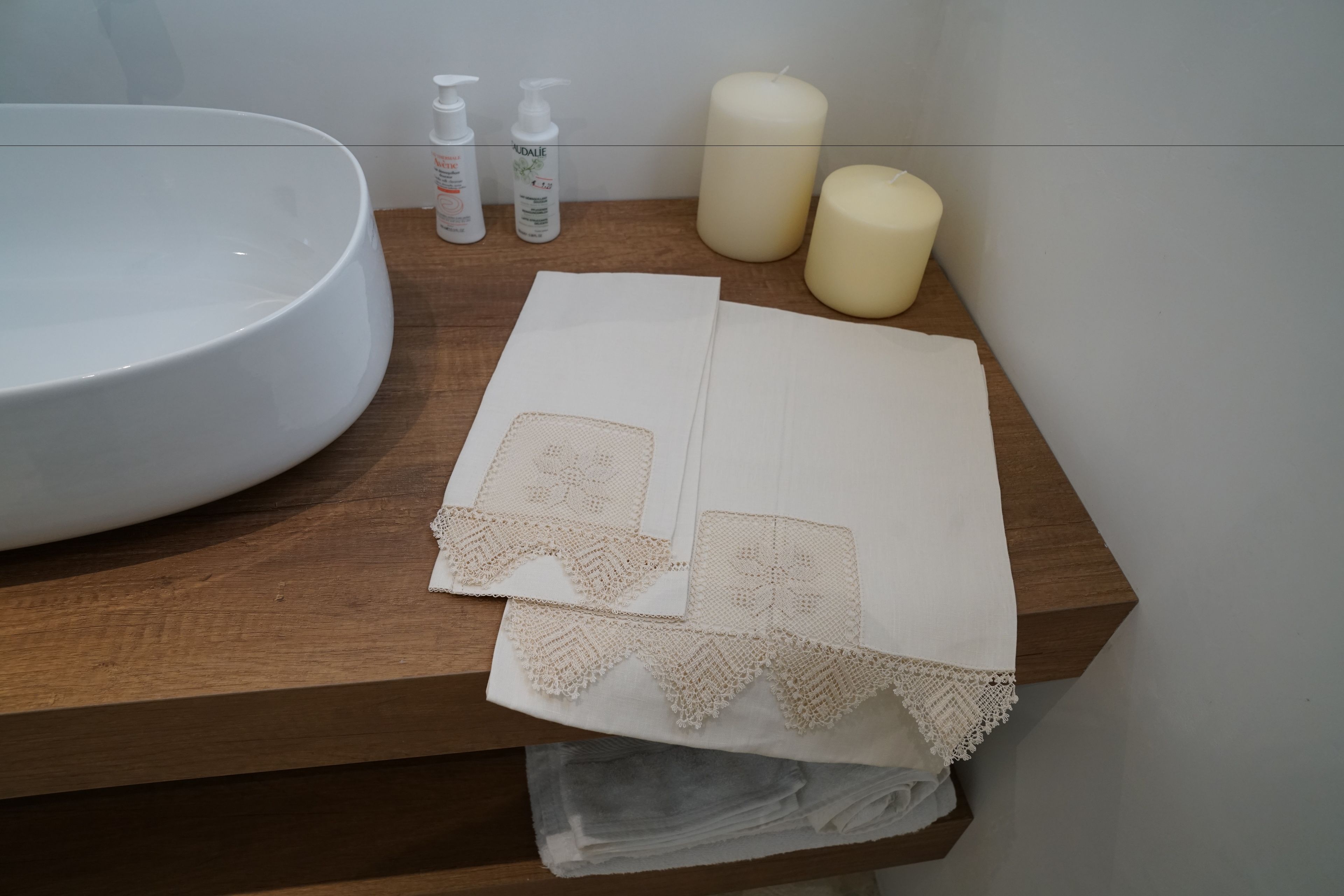 Een badkamermeubel met een wit wastafel, twee kaarsen en toiletartikelen op een houten aanrecht.