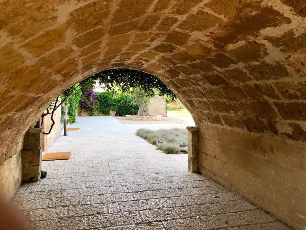 Un couloir voûté en pierre, avec un chemin pavé menant à un jardin.