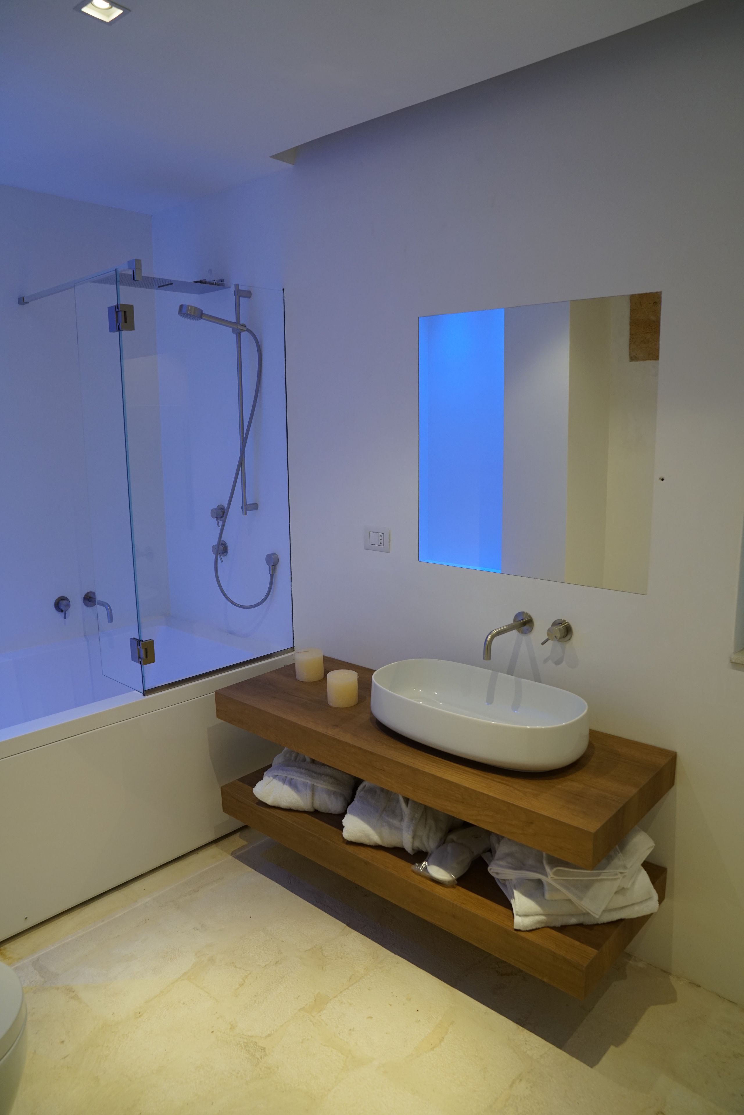 A modern bathroom with a glass-enclosed shower, a white sink with a wooden vanity, and a mirror above the sink.