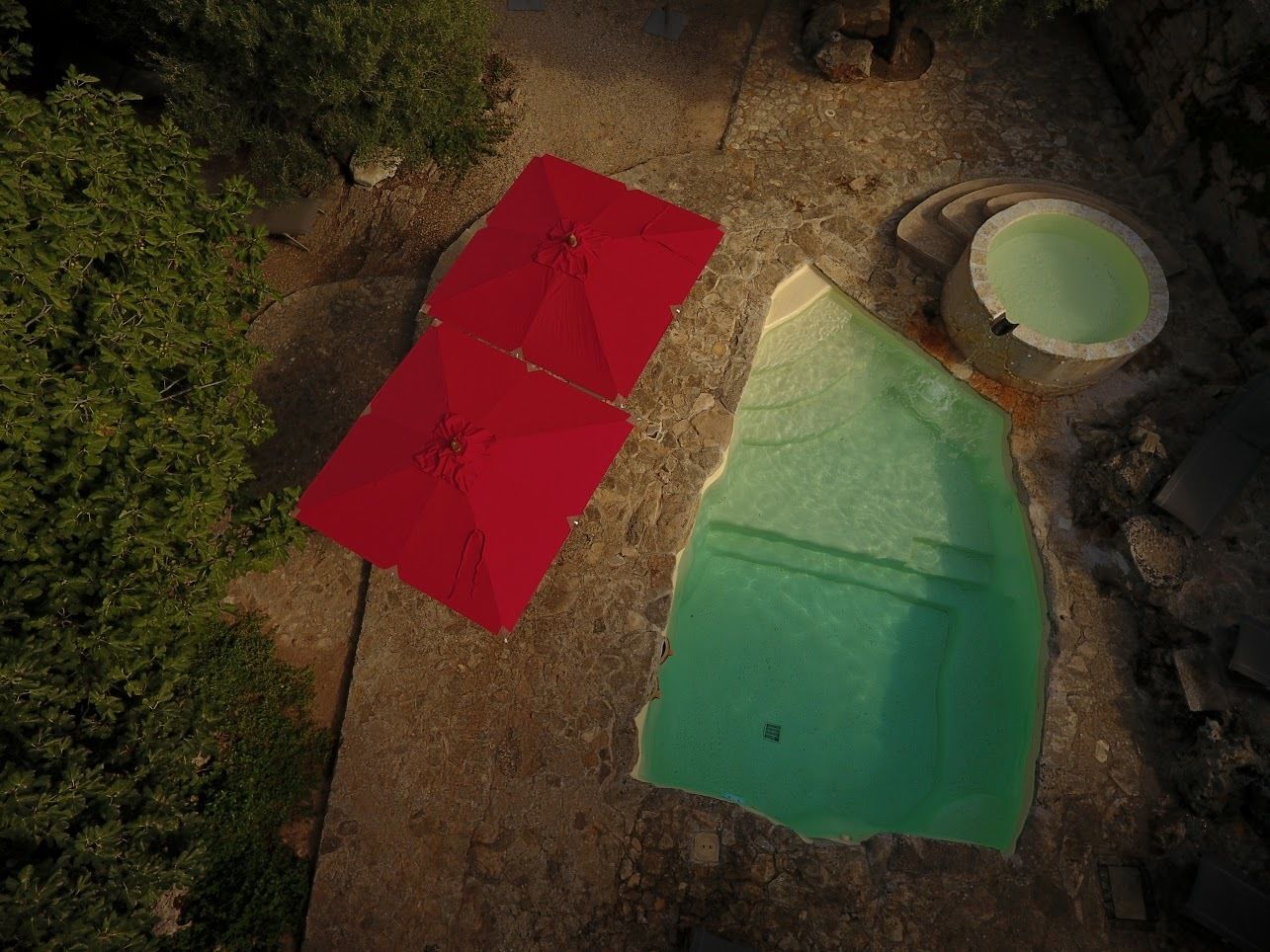 Luftaufnahme eines Poolbereichs mit zwei roten Sonnenschirmen und einem grünen Pool.