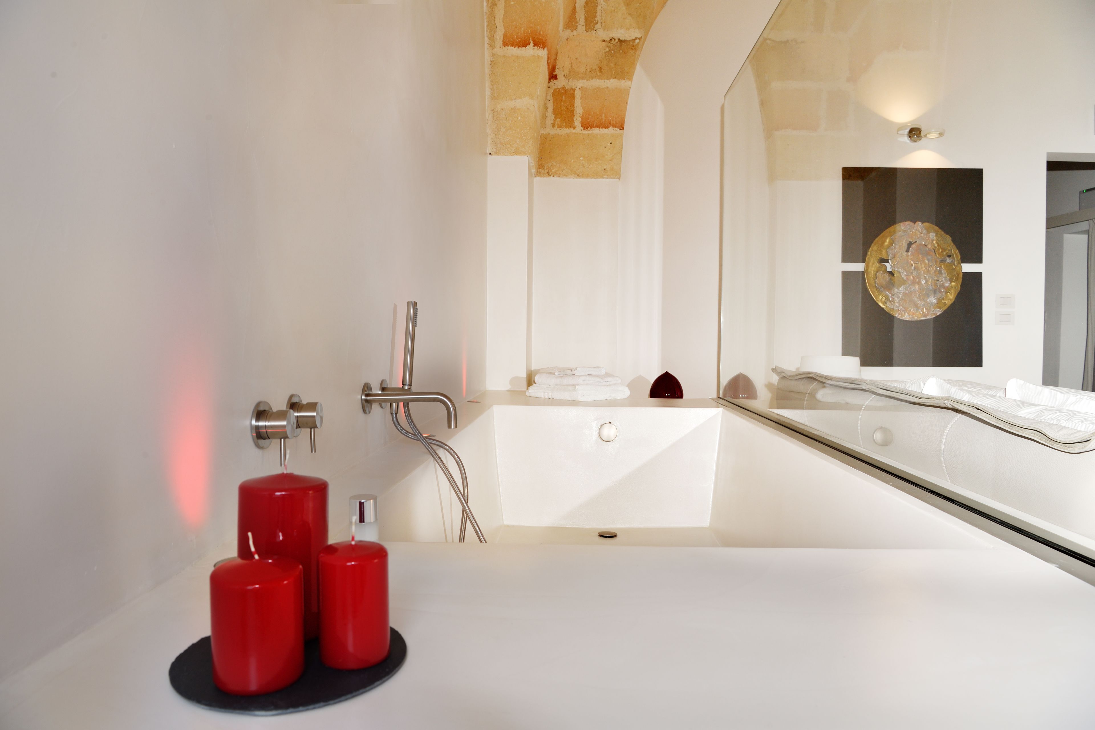 A modern bathroom with a bathtub, a large mirror, and red candles on a black tray.