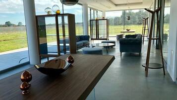 Amplia sala de estar con una mesa de madera, asientos y ventanas grandes que ofrecen vistas al exterior.