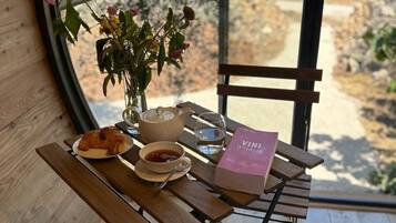 A wooden table with a book, a bowl of soup, a cup of tea, and a croissant.