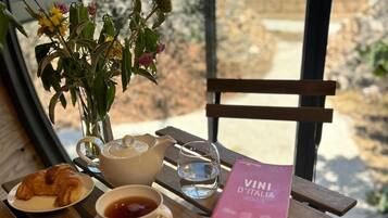 A dining table with a croissant, a bowl of jam, a glass of water, a teapot, and a book titled 'VINI D'ITALIA 2023'.