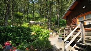 A wooden cabin with a wooden deck and a garden with various plants and flowers. - Les Vignes (Durbuy)