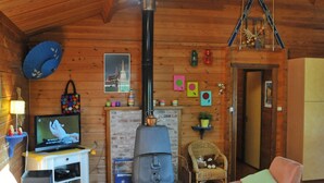 A cozy cabin interior with a wooden ceiling, a fireplace, a television, and comfortable seating. - Les Vignes (Durbuy)