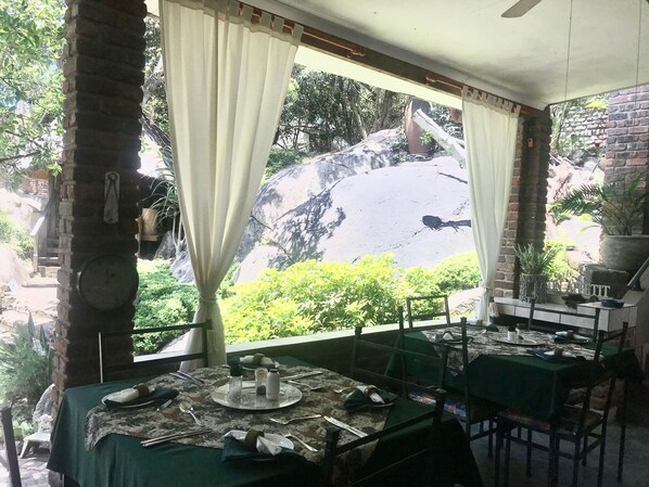 A dining area with a table set for two, a view of a rocky landscape, and a brick wall.