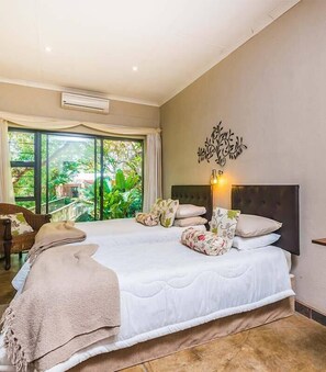 A bedroom with a large bed, a decorative wall piece, and a view of greenery through the window.
