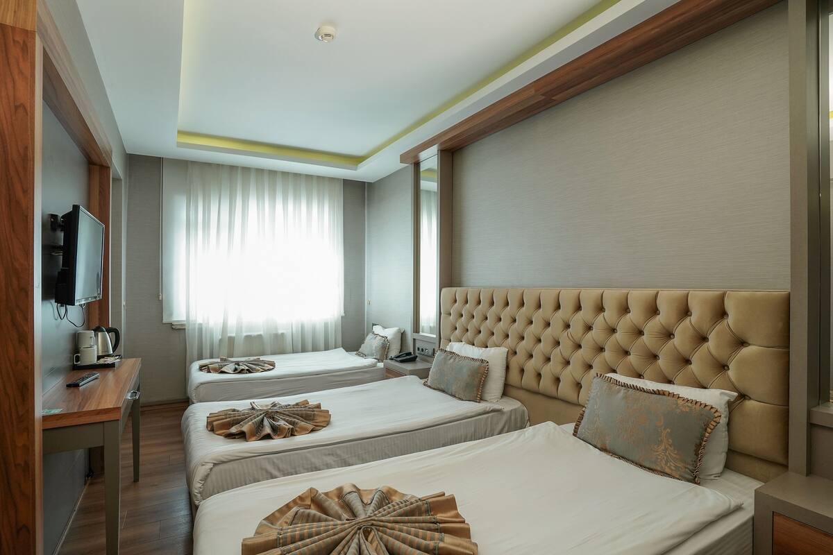 A hotel room with two beds, a TV, a desk, and a window with curtains.