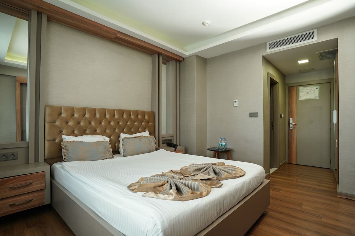 A hotel room with a large bed, a wooden headboard, a bedside table with a lamp, and a mirror.