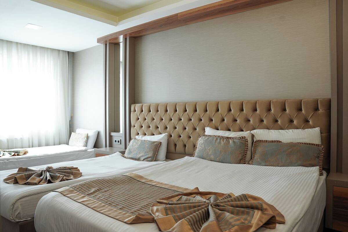 A hotel room with two beds, a large tufted headboard, and a view of the city.