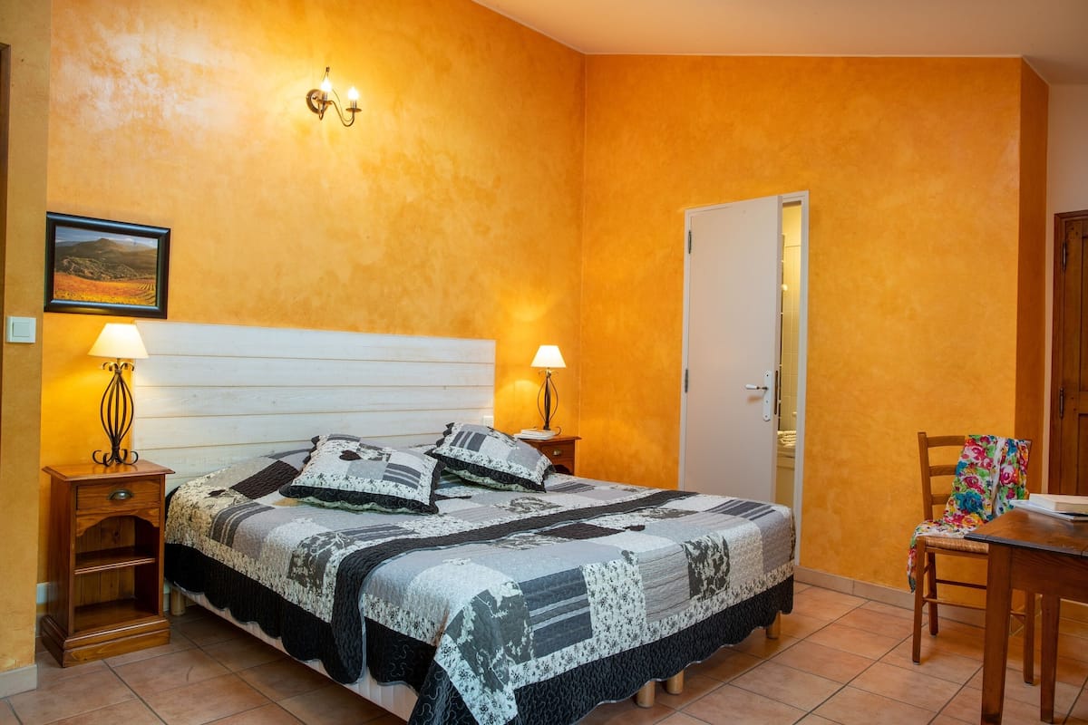 A bedroom with a large bed, two bedside tables with lamps, a wooden nightstand, a chair, and a door.