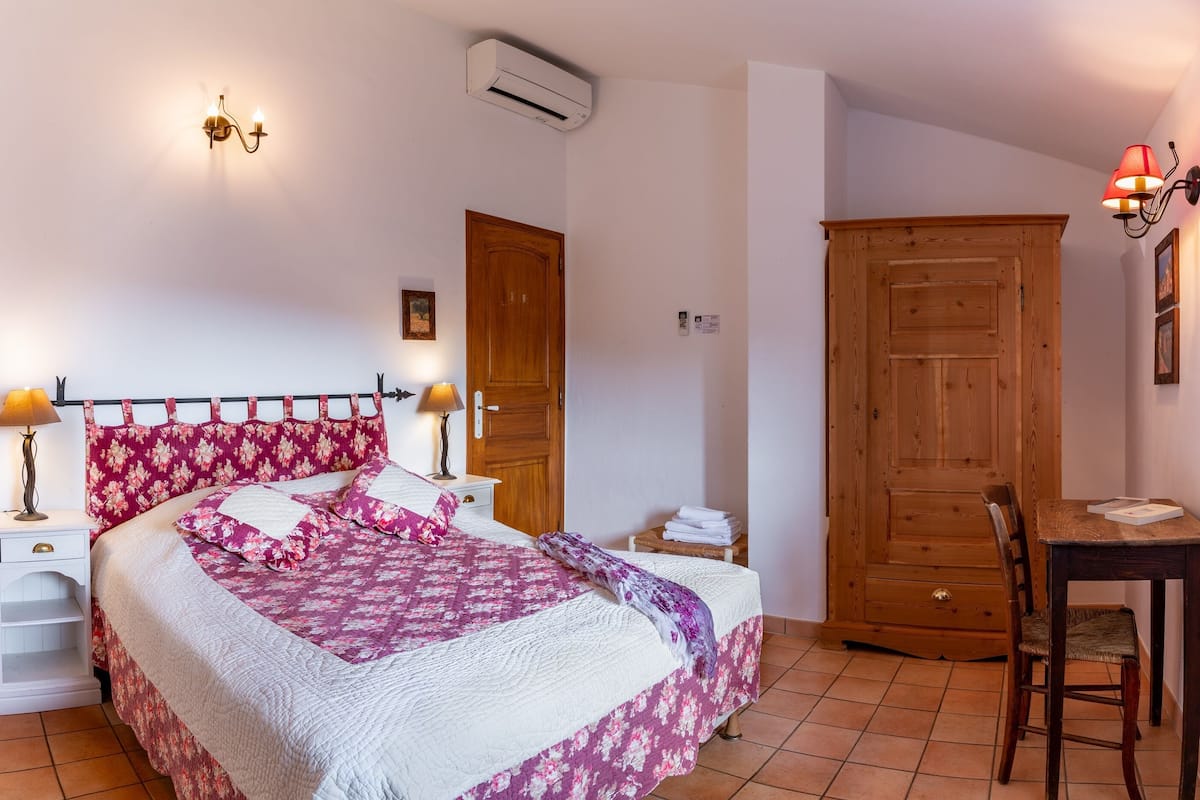 A bedroom with a bed, bedside lamps, a wooden wardrobe, a desk, and a chair.