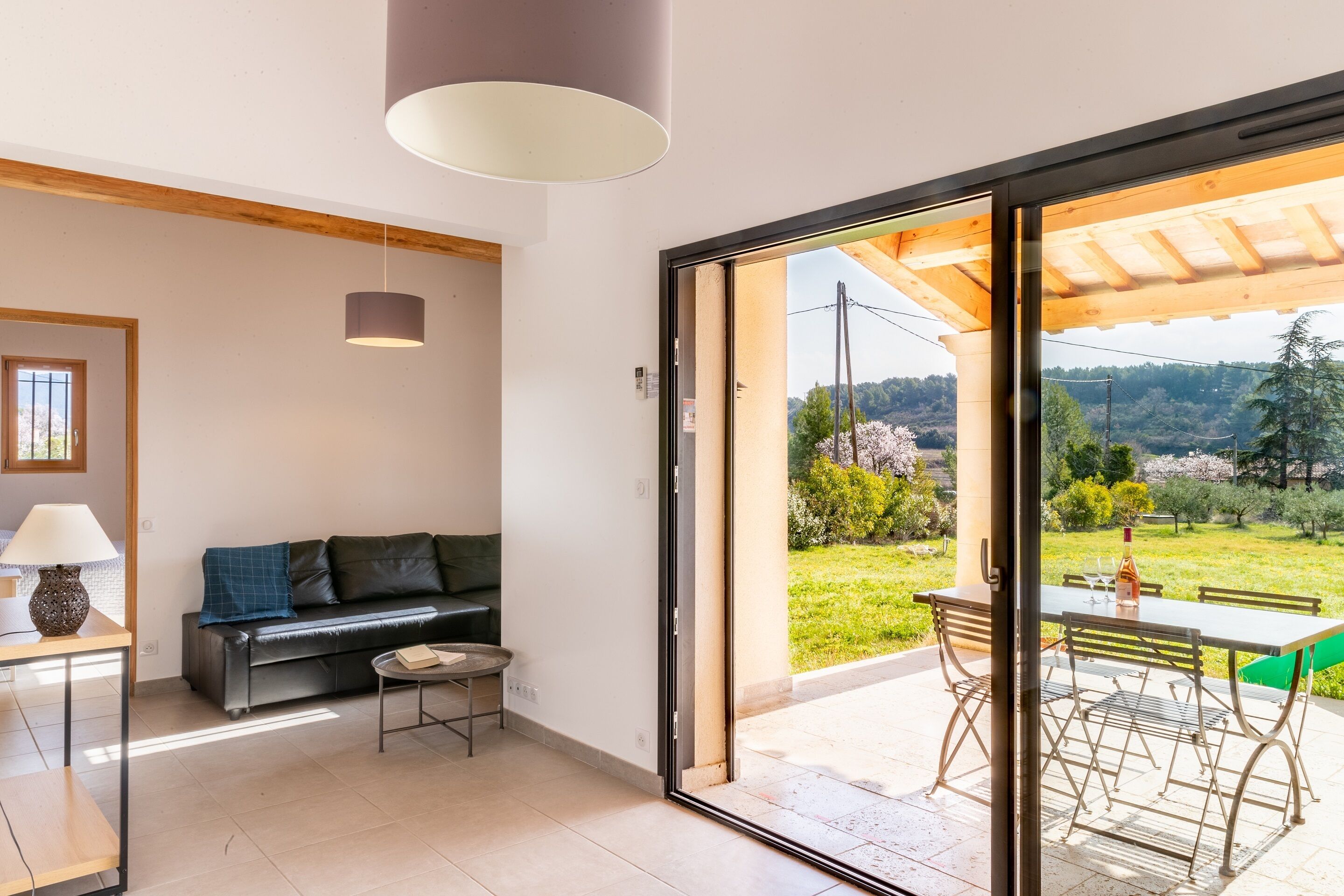 Una sala de estar moderna con un sofá, una mesita y una lámpara. Hay una puerta corrediza de vidrio que da a un patio exterior con una mesa y sillas.