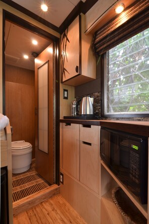 A compact kitchen with a microwave, kettle, and a window with a view of trees. - Seattle Glamping - Zen Den (Seattle)