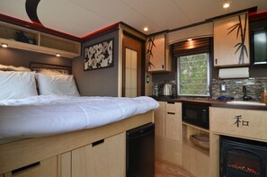A compact bedroom with a bed, a microwave, a small sink, and a fireplace. - Seattle Glamping - Zen Den (Seattle)
