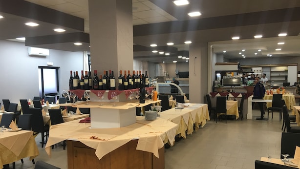 A restaurant with multiple tables, a wine display, and a kitchen area. - Il Calipso by Mago (Turbigo)