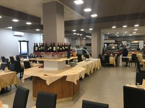 A restaurant with multiple tables, a wine display, and a kitchen area. - Il Calipso by Mago (Turbigo)