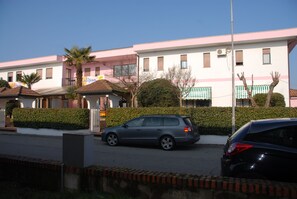 Um edifício com fachada rosa e branca, portão fechado e carros estacionados.