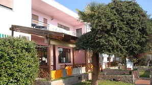 A pink building with a balcony and a large tree in front. - Il Calipso by Mago (Turbigo)