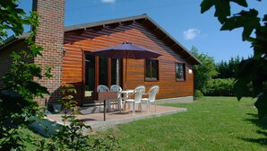 A wooden cabin with a brick chimney, a patio with a table and chairs, and a covered outdoor seating area. - La Tanière (Somme-Leuze)