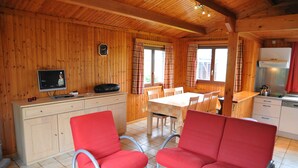 A wooden cabin interior with a dining area, kitchen, and a TV on a cabinet. - La Tanière (Somme-Leuze)