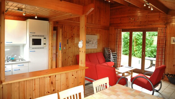 A wooden cabin interior with a kitchen, dining area, and a red sofa. - La Tanière (Somme-Leuze)
