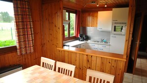 A wooden cabin with a kitchen area, dining table, and chairs. - La Tanière (Somme-Leuze)