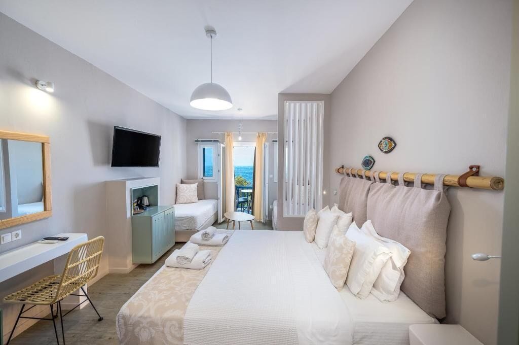 A hotel room with a bed, a desk, a chair, a television, and a view of the sea.