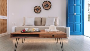 A room with a wooden coffee table, a sofa with patterned cushions, a blue door, and decorative wall art. - Blue Bay Resort Village (Andros)