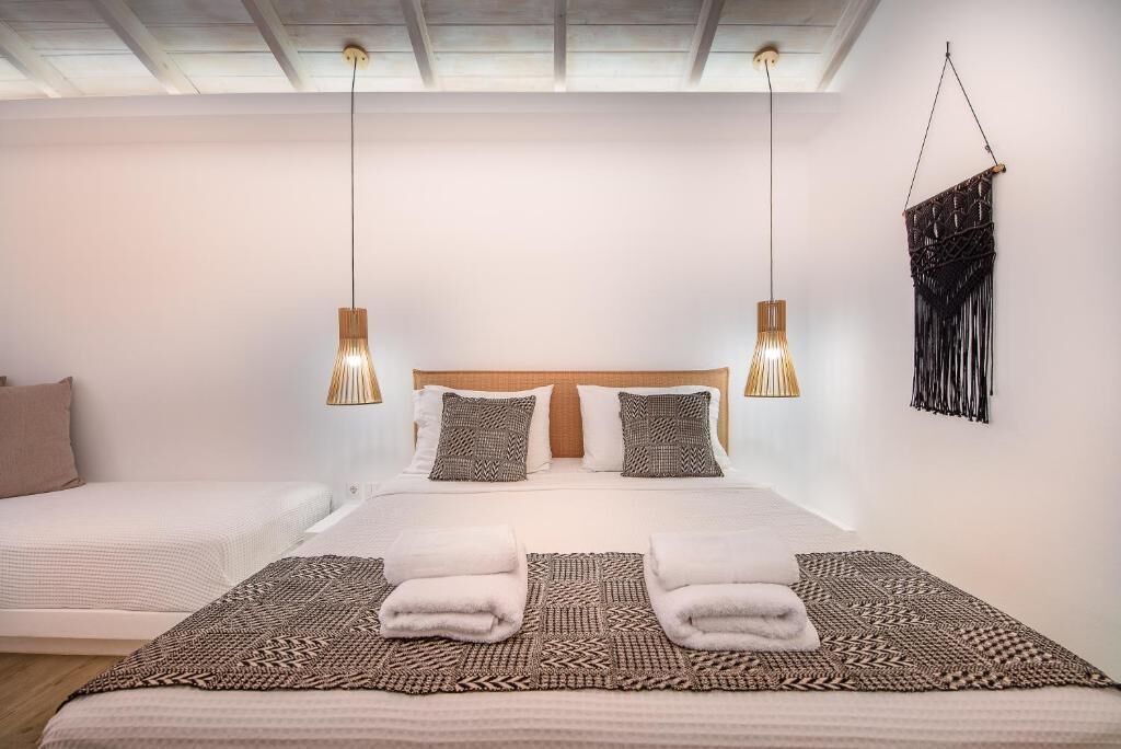 A double bed with a patterned bedspread, two bedside lamps, and a macrame wall hanging.